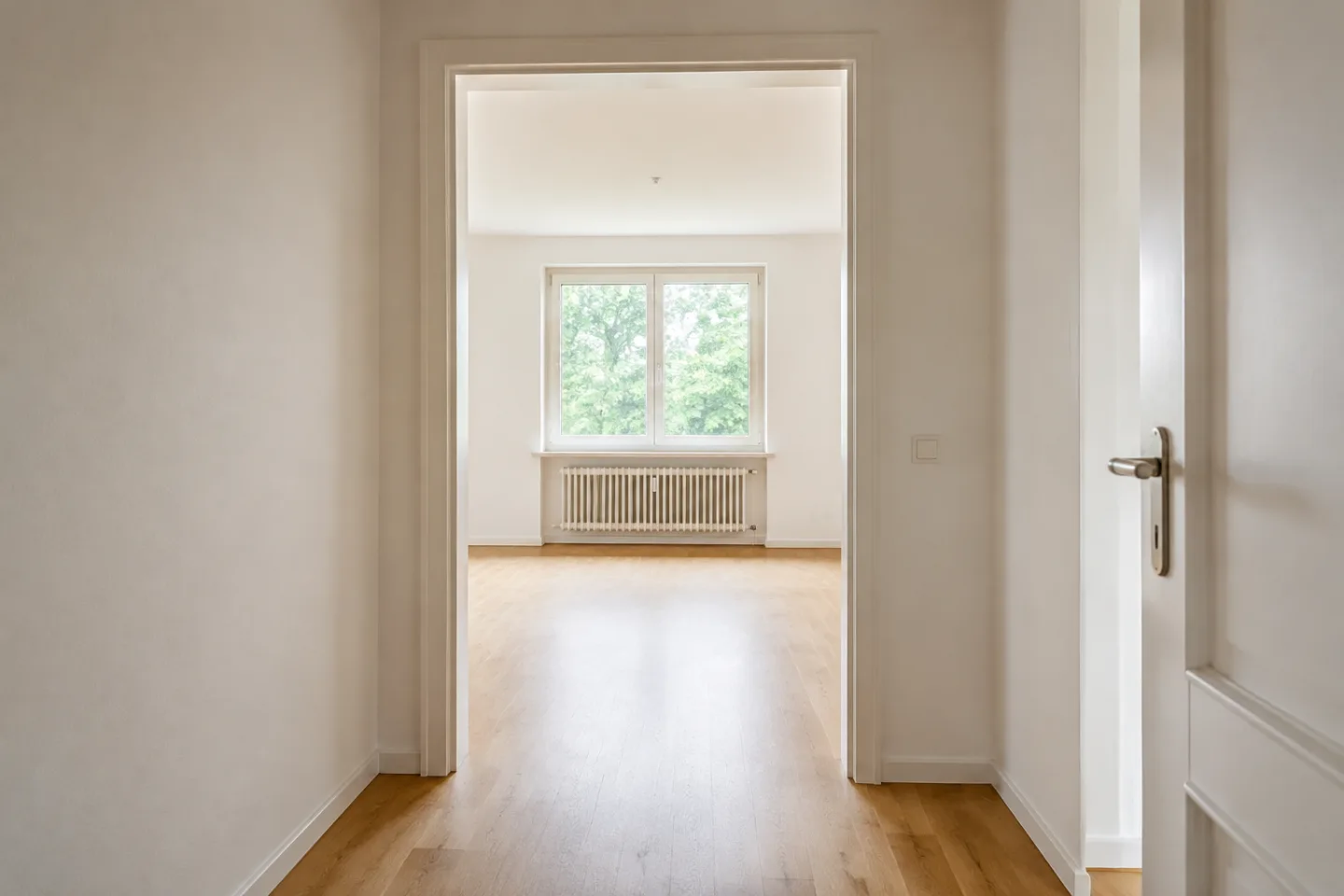 Blick durch den Flur in einen unmöblierten Raum mit Fenster und Heizkörper.