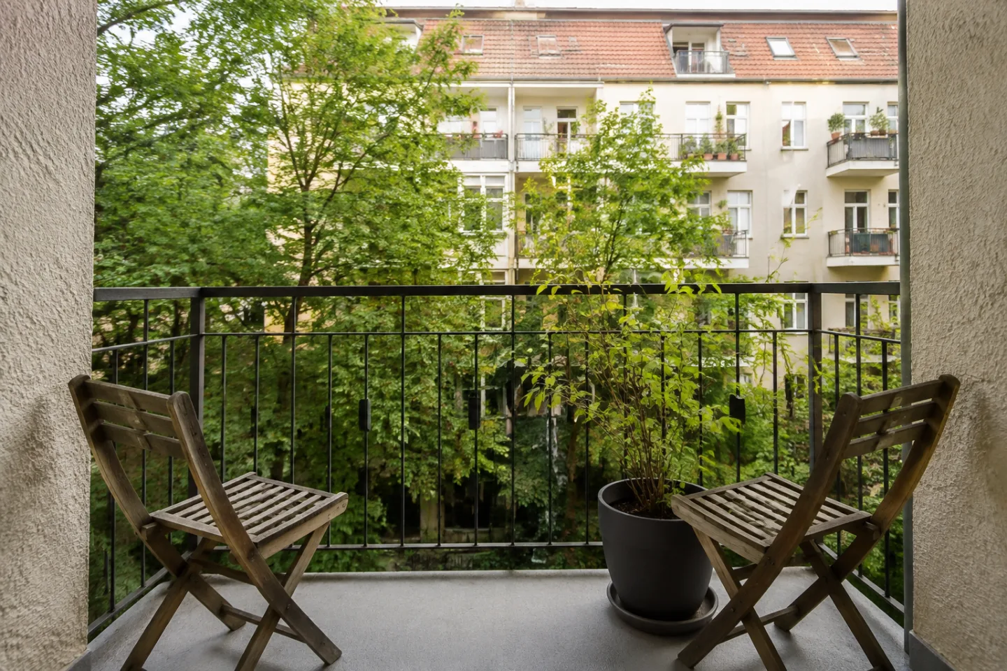 Zwei Holzstühle auf einem Balkon mit Blick auf einen begrünten gemeinschaftlichen Innenhof.